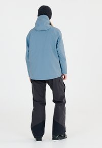 Hellblauer wasserdichter Parka mit Kapuze, kombiniert mit dunkelgrauen Cargo-Hosen, die am Saum einen kontrastierenden schwarzen Akzent aufweisen.