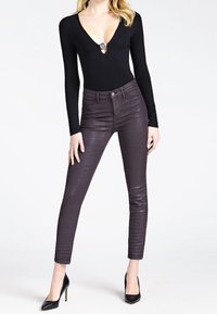 Bodysuit nero a maniche lunghe con scollatura a V profonda e dettagli argentati. Jeans skinny viola scuro con finitura lucida, abbinati a tacchi alti neri.