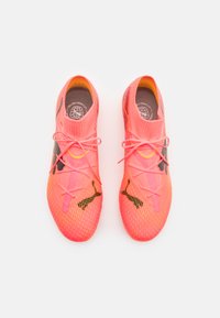Heldroze sportschoenen met een mesh-textuur, voorzien van zwarte accenten, dunne veters en een opvallend logo op de zijkanten.
