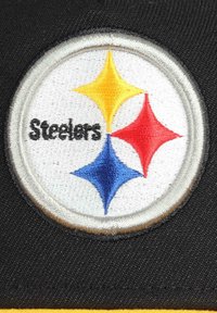 Schwarzer Stoff mit einem runden gestickten Patch auf weißem Hintergrund und einem stilisierten Logo von drei Diamanten in Gelb, Rot und Blau.