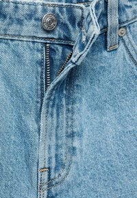 Svetlomodré džínsy z denimu majú zips a gombíkovú schránku, s viditeľným šitím a textúrovými detailmi, vrátane vyblednutých oblastí a vreciek.