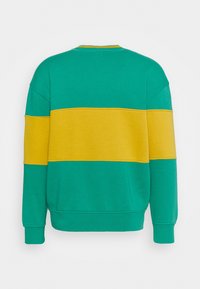Sweatshirt vert avec une large bande horizontale jaune traversant la poitrine et les manches, vue de dos.