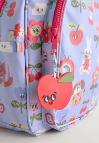 Sac à dos violet clair avec des fleurs, des animaux, des fruits colorés de dessin animé et un charm en forme de pomme rose avec un visage souriant.