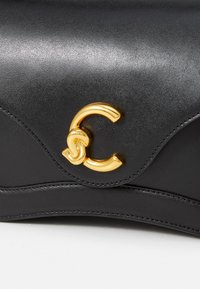 Borsa a tracolla in pelle nera con un design curvo, dettagli in metallo dorato e una chiusura con logo in evidenza. Texture liscia con un leggero lucido.