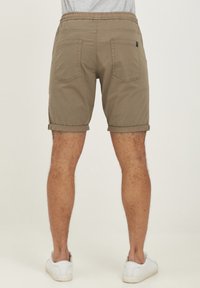 Shorts kaki avec revers roulés, taille élastique et deux poches arrière. Fabriqués en tissu de coton doux. Baskets blanches visibles.