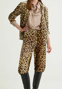 Blazer in velluto con fantasia leopardata e pantaloni abbinati, camicetta beige con bottoni, abbinati a stivali neri testurizzati fino al ginocchio.