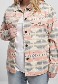 Button-up jacket in pastel colors with geometric patterns. Features two front pockets, a collar, and metal snap buttons. Fabric has a textured finish.