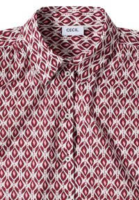 Chemise à col avec motif géométrique en losange rouge et blanc et boutons blancs, étiquetée avec le nom de la marque CECIL à l'intérieur du col.