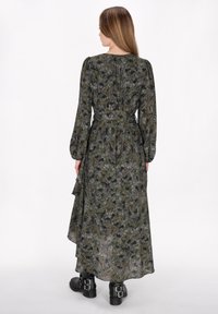 Abito floreale di colore verde scuro, con maniche lunghe, vita sfiancata e orlo a strati. Realizzato in tessuto leggero con una consistenza morbida.