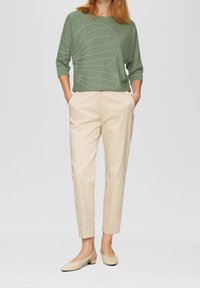 Zielony sweter z białym wzorem, beżowe spodnie o tapered fit oraz jasnobeżowe buty typu slingback. Gładkie faktury i luźny krój.