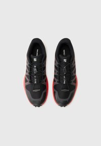 Black athletic shoes with red accents, synthetic upper, textured surface, laces with toggle, and a thick white sole.
