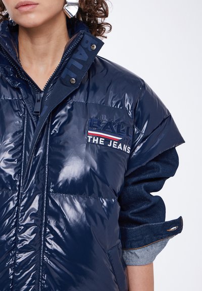 Jūros jėgos pūkinė striukė blizgiu paviršiumi, su aukštu apykakle, užtrauktuku ir siuvinėtu logotipu ant krūtinės. Džinsiniai akcentai rankovėse.