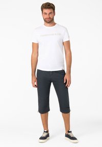 Weißes Kurzarm-T-Shirt mit "TIMEZONE & CO" in heller Schrift; dunkle, gekürzte Hosen; marineblaue Sneakers mit weißen Sohlen; lässiger Schnitt.