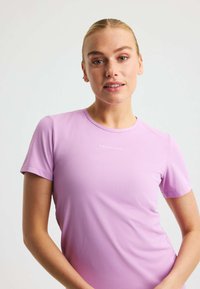 Lätt, ärmlös atletisk topp i ljusrosa med en texturerad yta och rundad halsringning. Har en logotyp på framsidan i mitten.