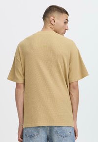 Camiseta beige texturizada de corte holgado, con mangas cortas y escote redondo, combinada con jeans de color azul claro.