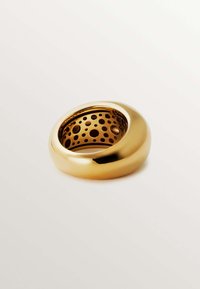 Anillo de oro con superficie exterior lisa, que presenta un interior texturizado con recortes circulares. Acabado pulido, forma redondeada y apariencia brillante.