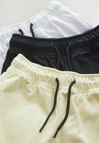 Tre par atletiska shorts i svart, vit och ljusgul. Varje par har ett elastiskt midjeband med svarta dragsnöret och en slät textur.