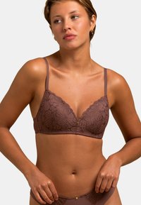 Soutien-gorge en dentelle marron avec un motif floral, présentant des bords scallopés, des bretelles ajustables, et un petit accent doré au centre.