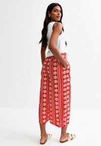 Rote gemusterte Weitbein-Hosen mit weißen Blumenmotiven und vertikalen Streifen, ausgestattet mit seitlichen Taschen und einer lockeren Passform. Kombiniert mit einem weißen Oberteil.