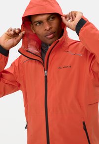 Rode waterdichte jas met een capuchon, voorzien van ritszakken en reflecterende accenten. Gemaakt van lichtgewicht materiaal, met een gladde textuur.