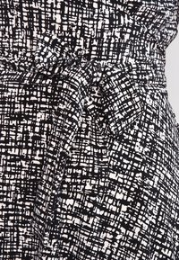 Svart och vit mönstrad tyg med en strukturerad yta. Har ett knutet bälte i midjan, med lös passform och varierande rutnätsmönster.