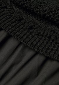 Nahaufnahme von schwarzem Stoff mit gerippter Stricktextur über glattem Gewebe mit gerafften Falten.