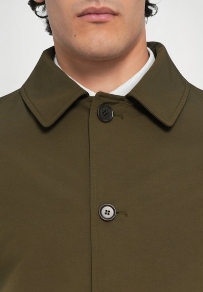 Abrigo de tela verde oliva con un cuello clásico, dos botones negros y detalles de costura visibles. Textura suave y diseño minimalista.
