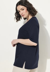 Námořnická modrá halenka s krátkým rukávem, V-výstřihem a bočními rozparky, vyrobená z měkké látky. Design má uvolněný střih a minimální detaily.