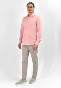 Lichtroze overhemd met lange mouwen en een spitse kraag, gecombineerd met lichtbeige broeken en grijze instapschoenen. Gladde textuur.