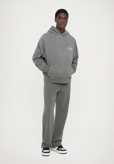 Gray hoodie with a kangaroo pocket and embroidered logo, paired with matching sweatpants. Fabric appears soft with a relaxed fit.