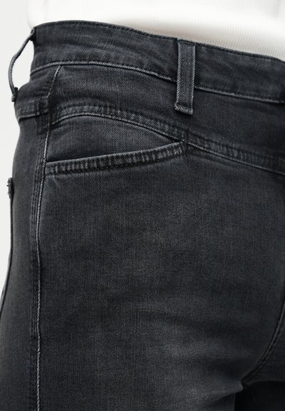 Κοντινό πλάνο στη μέση και πίσω τσέπη ενός μαύρου τζιν παντελονιού, που φοριέται με λευκό τοπ, εμφανίζοντας τη θηλιά της ζώνης και τις ραφές.