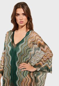 Proziran kimono pokrivač s zigzag uzorkom u zelenoj, bež i smešnoj boji, s dubokim V-izrezom i širokim rukavima za fluidno kretanje.