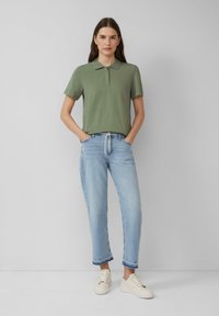 Jasnozielona koszulka polo z kołnierzykiem i guzikami, zestawiona z jasnoniebieskimi dżinsami o prostym kroju i postrzępionych nogawkach. Beżowe trampki.