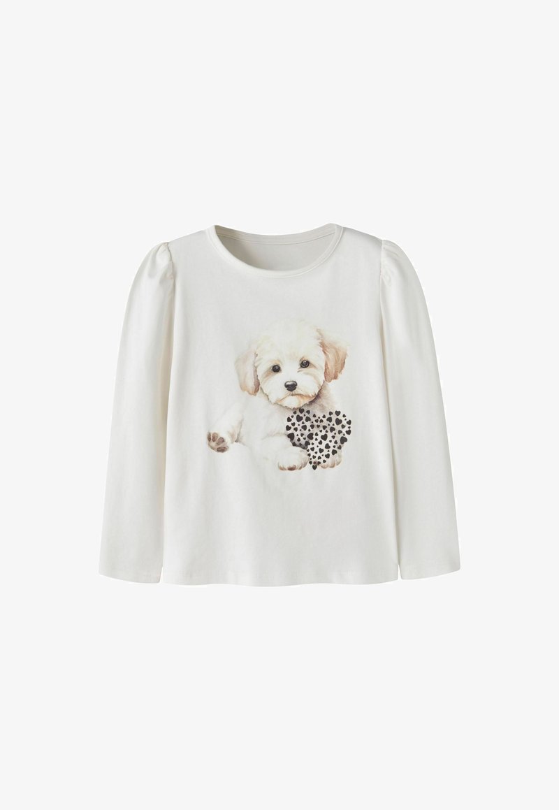 Chemise blanche à manches longues avec épaules bouffantes, présentant un graphisme d'un petit chiot blanc tenant un cœur noir et blanc tacheté.