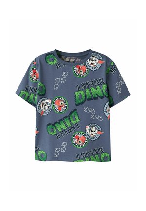 Chemise enfant à manches courtes bleue avec texte vert "I speak Dino", empreintes de dinosaures et visages d'animaux de dessin animé en patchs circulaires.
