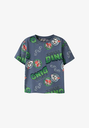 Chemise enfant à manches courtes bleue avec texte vert "I speak Dino", empreintes de dinosaures et visages d'animaux de dessin animé en patchs circulaires.