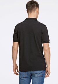 Polo nero con colletto classico, maniche corte e dettagli in maglia. Indossato con jeans blu, che mostrano un tessuto testurizzato.