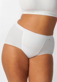 Perizoma bianco a vita alta in cotone con bordi scallop, caratterizzati da un design semplice e una piccola etichetta con logo sul lato. Texture morbida e liscia.