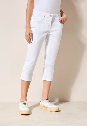 Weiße, aus Baumwolle gefertigte, cropped Hosen mit taillierter Passform, vorne Taschen und umgeschlagenen Säumen, kombiniert mit weißen Sneakers.