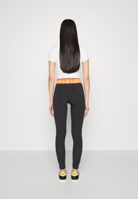 Čierne legíny s širokým oranžovým pásom s logom adidas, skombinované s bielym tričkom s krátkym rukávom a čierno-žltými teniskami.