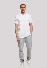 White cotton t-shirt paired with gray sweatpants. The outfit features a relaxed fit, with elastic cuffs on the pants and white sneakers.