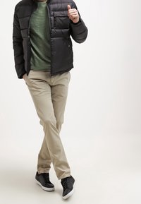 Mustat puhvijakke, vihreä t-paita, behesit housut ja mustat lenkkurit. Takissa on vaakasuoraa ommelta ja vetoketjusuljenta.