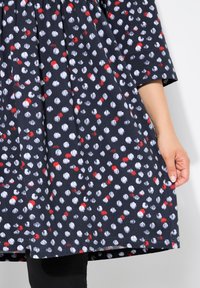 Vestido navy con un patrón de puntos rojos y blancos, mangas cortas y una cintura fruncida. Fabricado en una tela ligera con una textura suave.