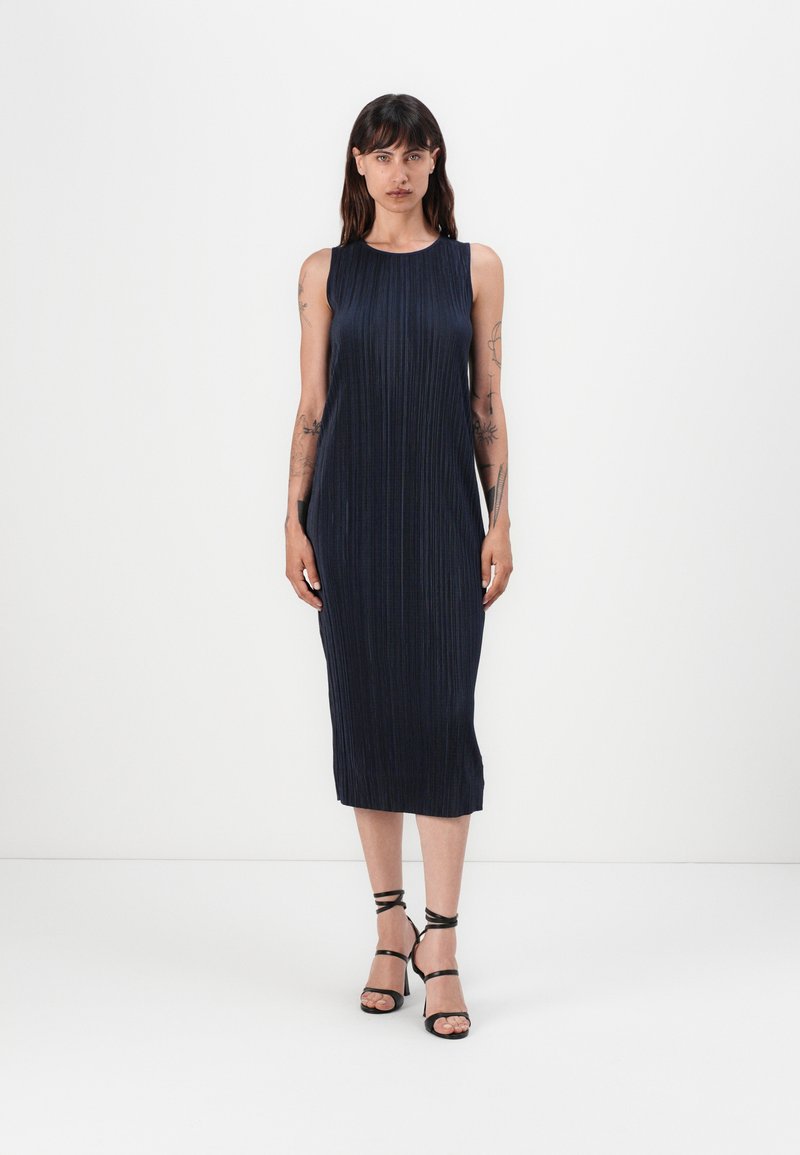Mekko, tummansinisestä, hihattomasta, laskostetusta midi-mallista, jossa on pyöreä pääntie. Mallilla on mustat, remmillä varustetut korkokengät. Yksinkertainen ja elegantti muotoilu.