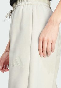 Hellgraue Jogginghose mit einem elastischen Bund und Kordelzug, ausgestattet mit einem strukturierten Logo und seitlichen Taschen. Weiches Material mit einer lockeren Passform.