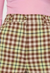 Karierte Hose in Braun-, Grün- und Pinktönen mit Knopfverschluss, Seitentaschen und strukturierter Stoffmusterung.