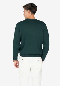 Suéter verde de punto con cuello y puños acanalados, de ajuste estándar. Llevado con pantalones cargo blancos.