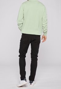 Lichtgroene trui met lange mouwen, gecombineerd met slim-fit zwarte jeans. Witte sneakers met marineblauwe accenten maken de outfit compleet.