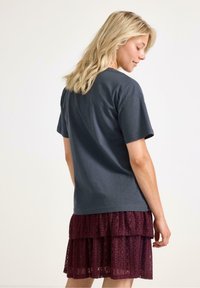 Grå bomulds T-shirt med korte ærmer, parret med en lagdelt burgunder blonde nederdel med et struktureret mønster. Synlige kantbånd og syningsdetaljer.