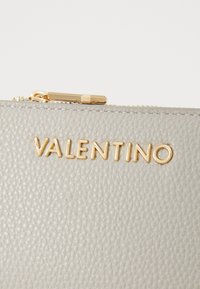 Borsa in pelle grigia con texture, con hardware e zip dorati, caratterizzata dal logo "VALENTINO" impresso sul davanti.